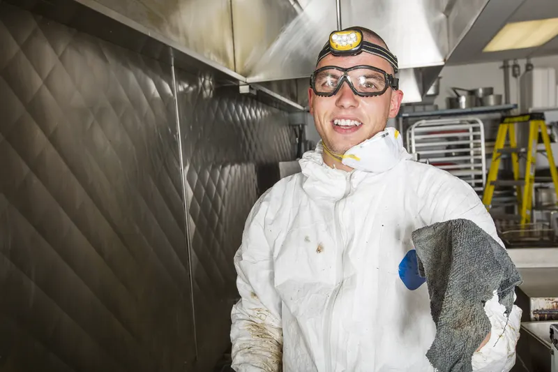 Commercial cook line pulled away from a tiled wall with the floor and wall behind the fryers exposed for degreasing