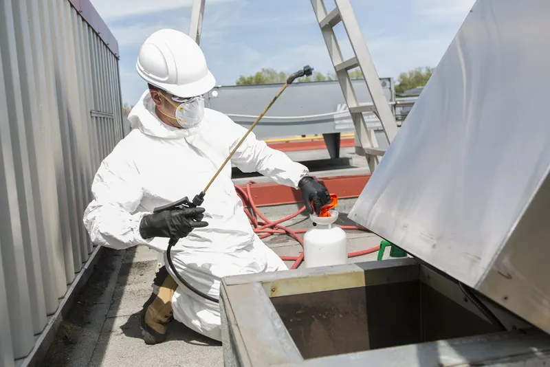 Upblast kitchen exhaust fan tipped back on a hinge kit on a flat commercial roof with the wheel and housing exposed for cleaning